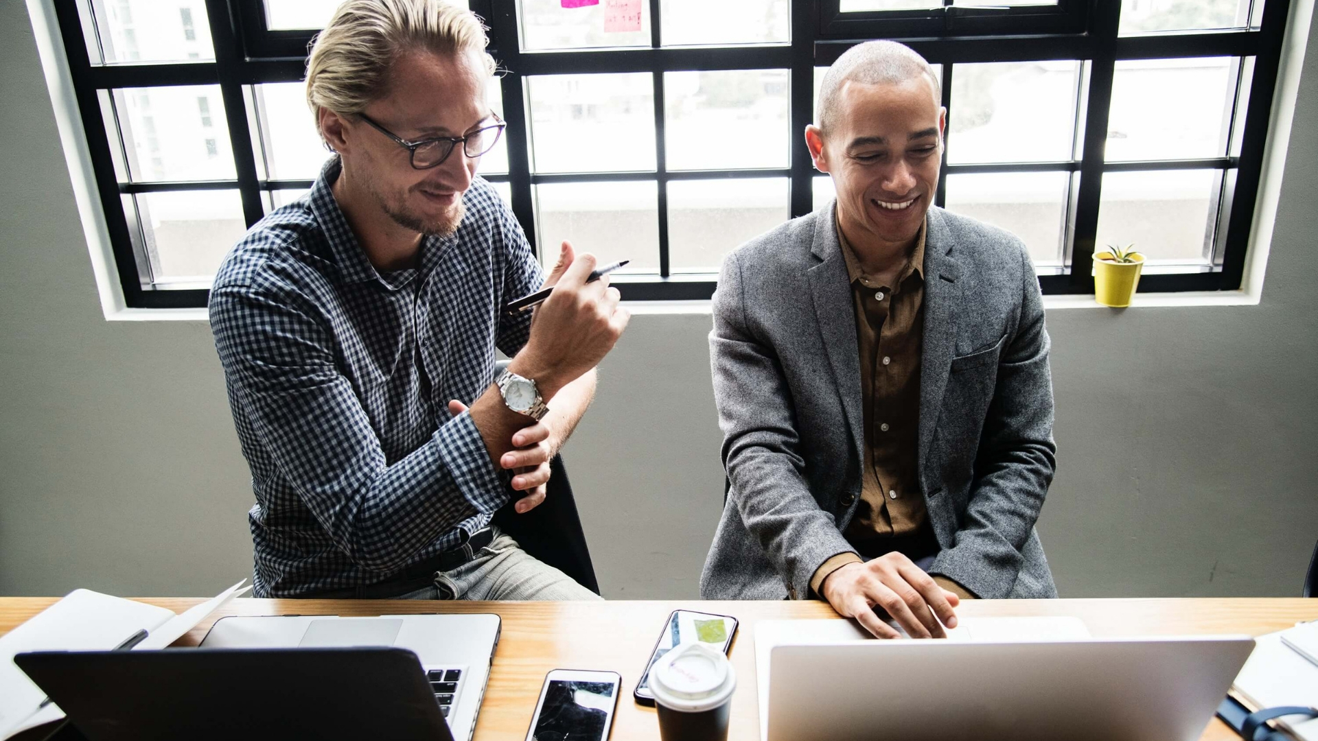 Two men laughing while working on their laptops